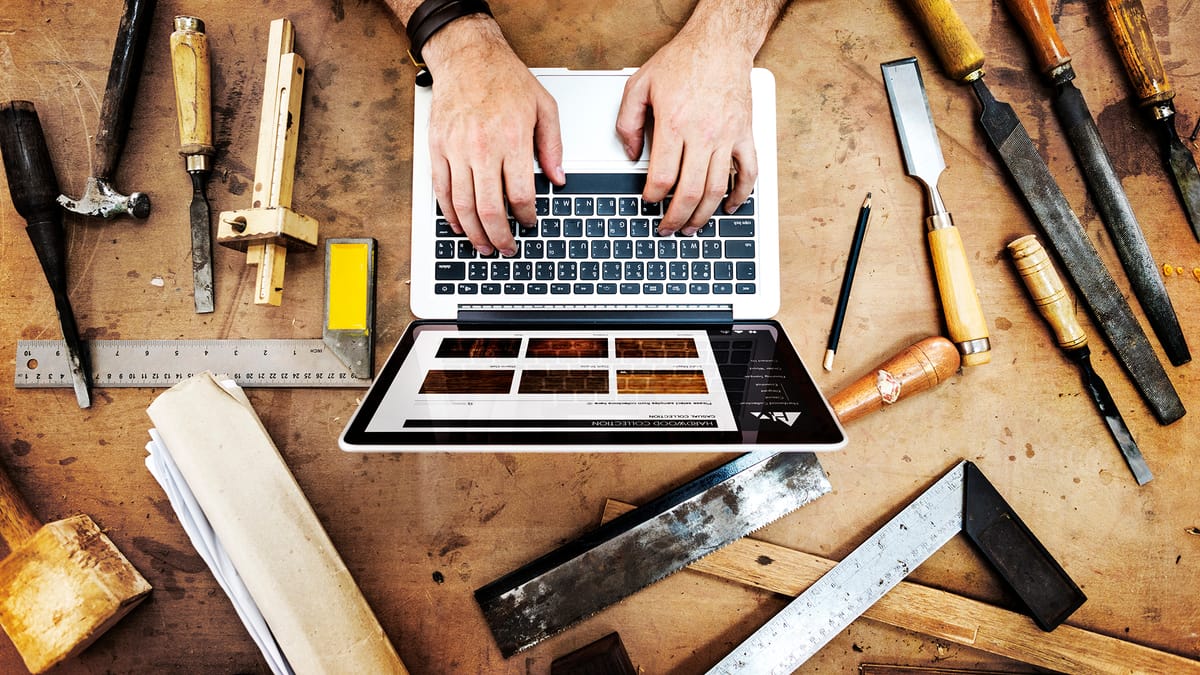 Artisan sur un laptop affichant des échantillons de bois, entouré d'outils de menuiserie sur un établi en bois